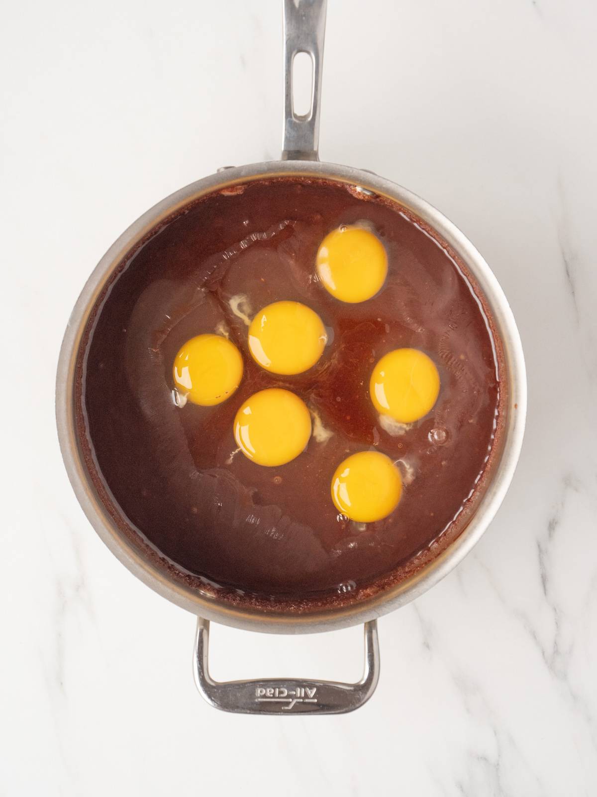 A medium pot with molten chocolate, sugar and butter in a smooth mixture and eggs just added.