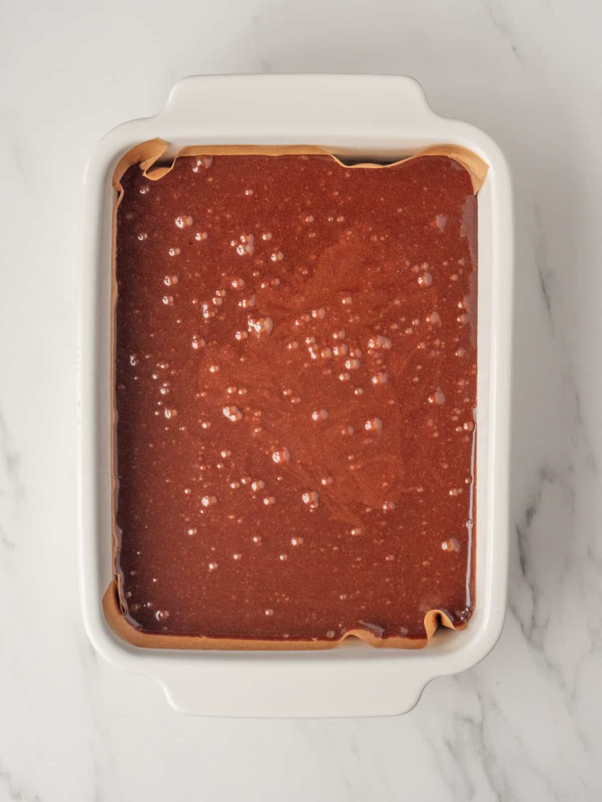 A white rectangular pan lined with parchment paper filled with brownie batter.