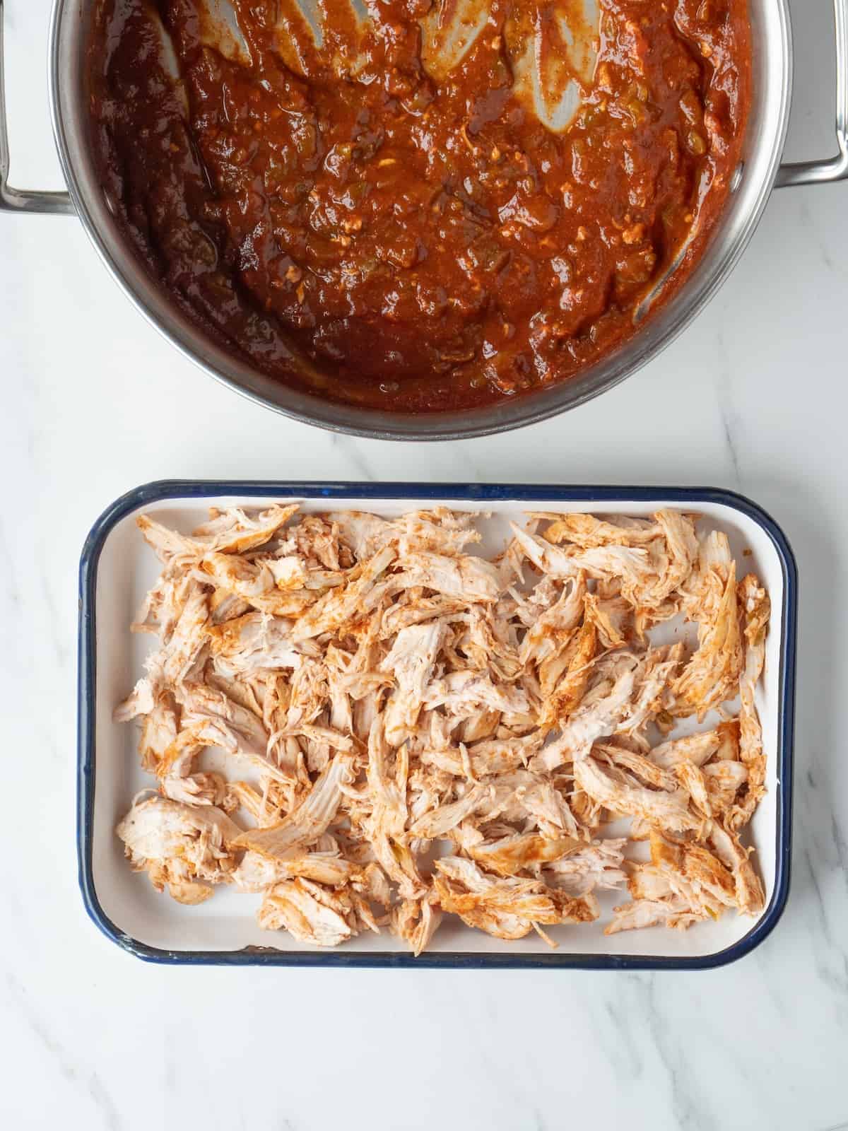 A rectangular dish with shredded chicken, along with a pot with the cooked enchilada sauce with the chiles.