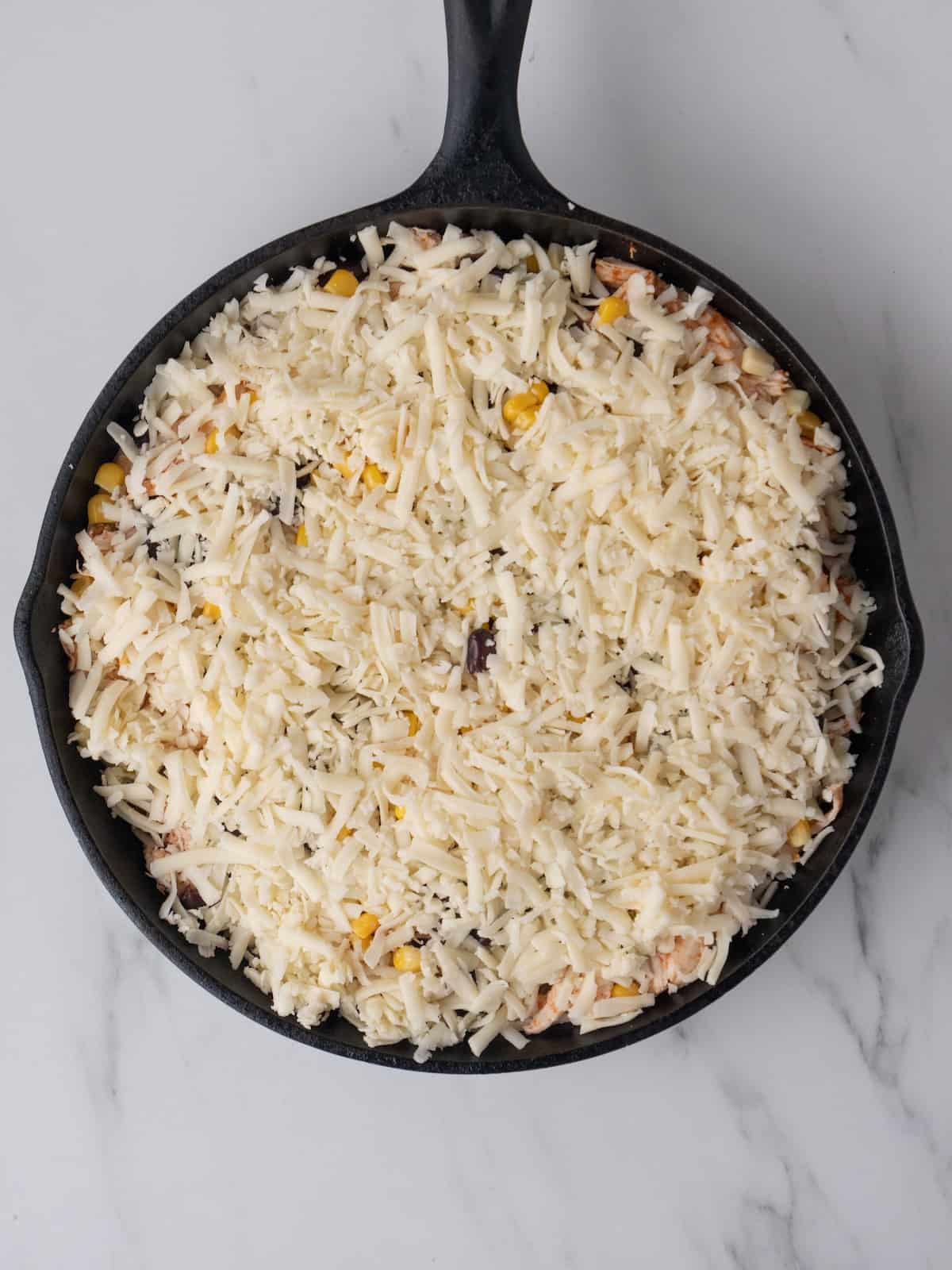 A skillet with chipotle chicken enchilada bake assembled and ready to be baked.