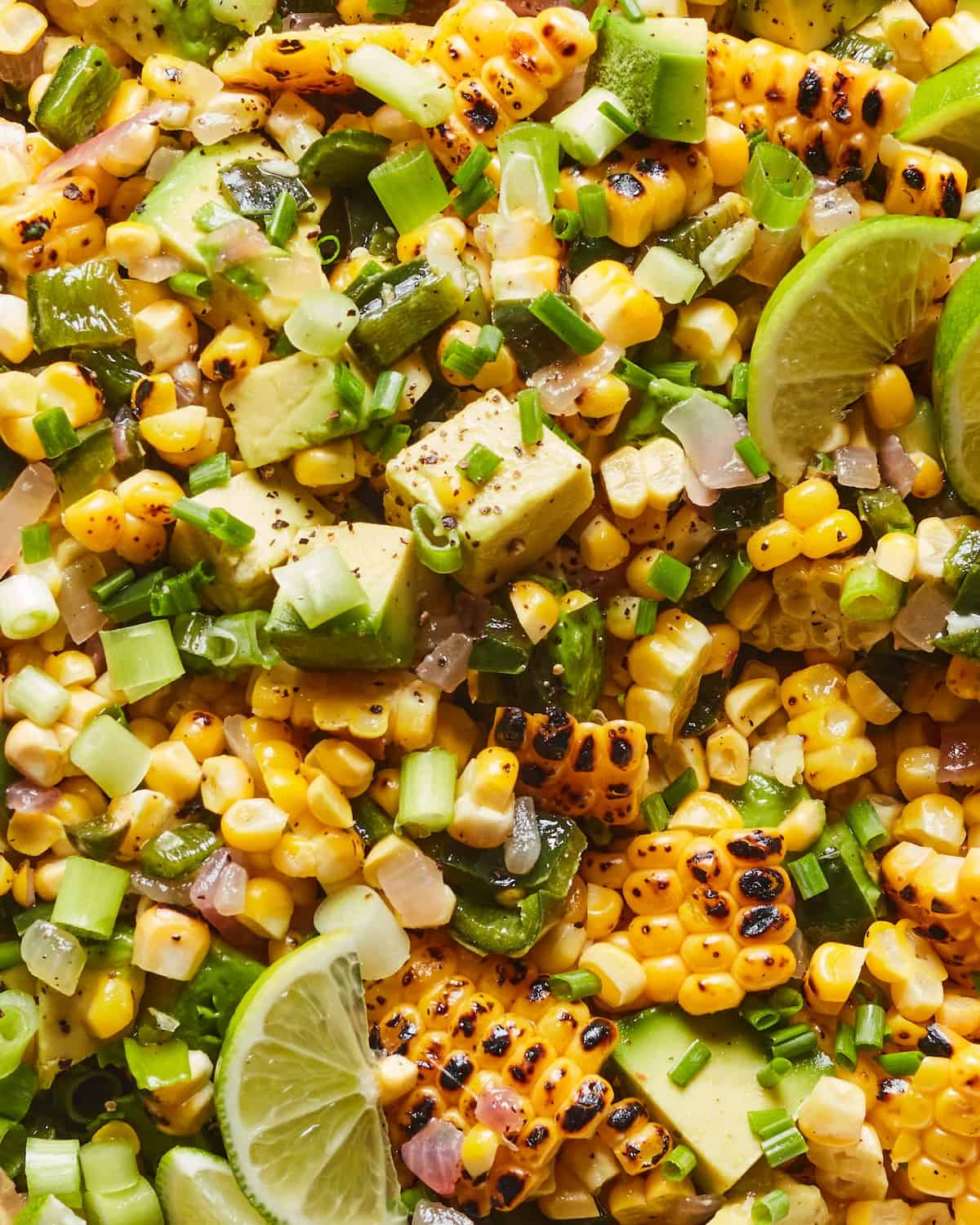 An overhead close-up shot of avocado corn salad, with lime wedges.