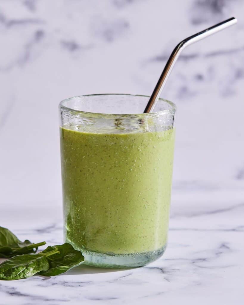 A drinking glass with breakfast spinach smoothie, and a metal straw.