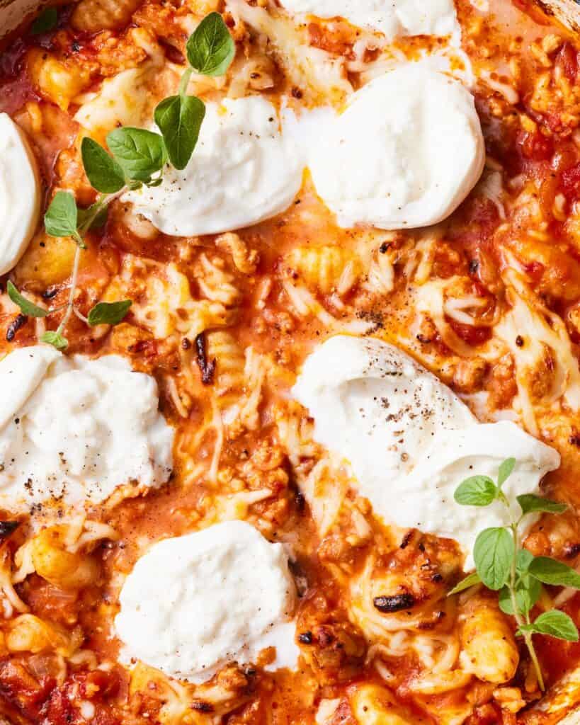 An overhead close-up shot of a baked chicken parmesan gnocchi topped with burrata and garnished with oregano.