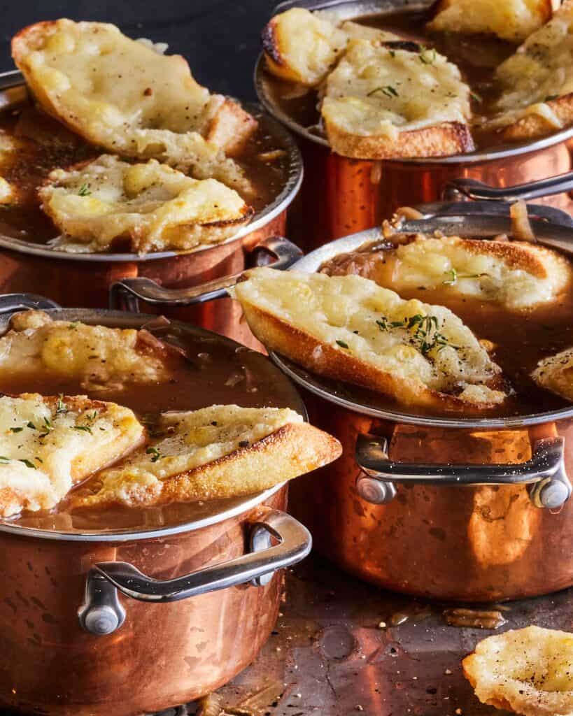Closeup shot of four copper plated ramekins of french onion soup topped with gruyère toasts.