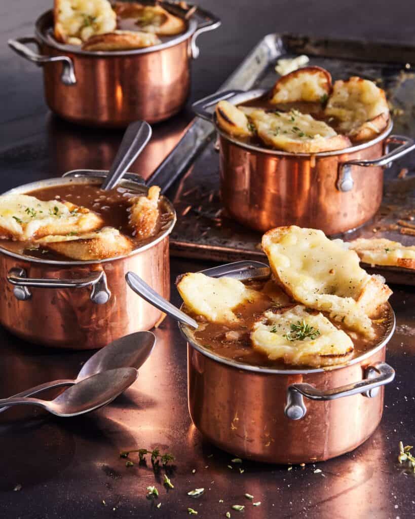 Four copper plated ramekins of french onion soup topped with gruyère toasts.