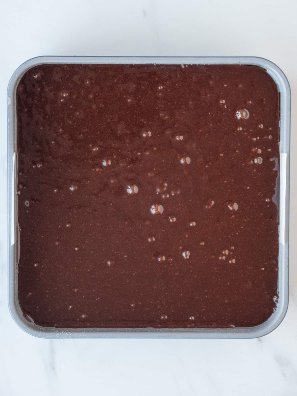 A parchment paper lined 9x9 baking pan with brownie batter poured in, ready to be added to the oven.