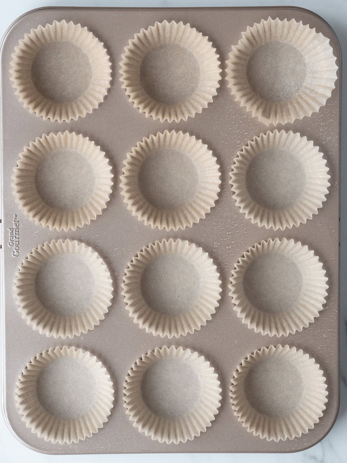 A 12 cupcake baking tray lined with cupcake liners and sprayed with non-stick baking spray.