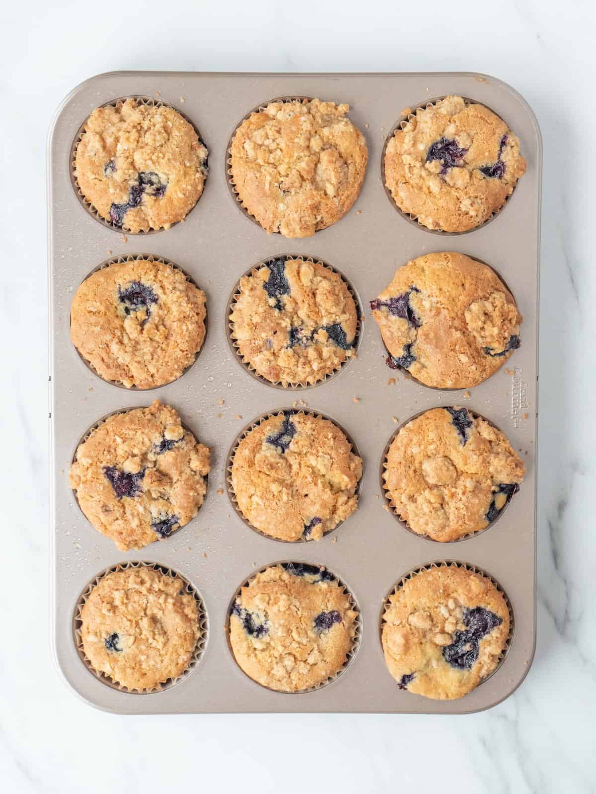 A cupcake baking pan with blueberry crumb muffins, baked and fresh out of the oven.