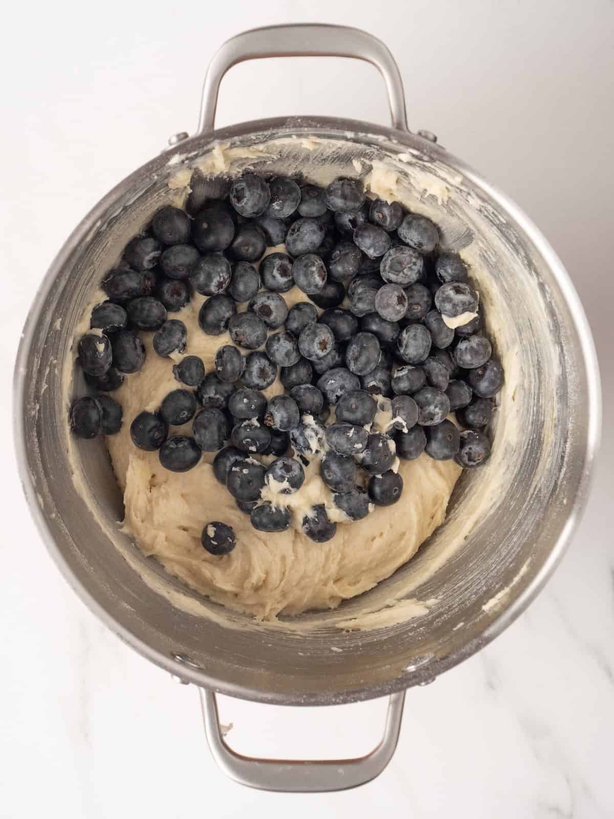 A stand mixer bowl with blueberry crumb muffins batter ready, with blueberries just added to be folded in to the batter.