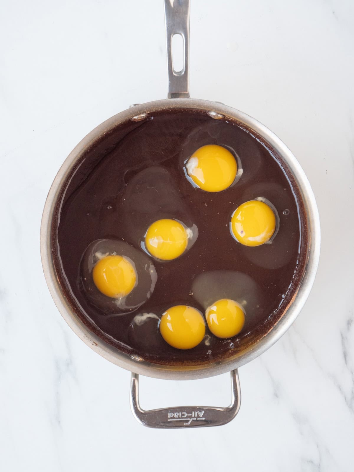 A saucepan with a batter of molten butter, chocolate chips, cocoa and white sugar, with eggs just added.