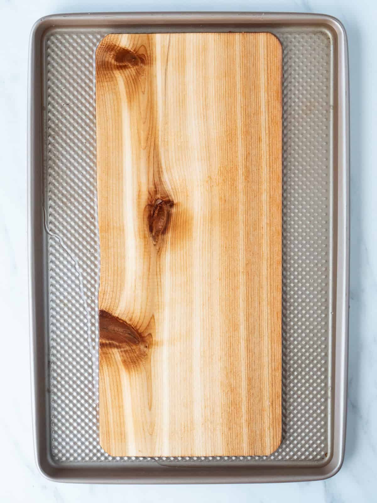 A baking sheet with a cedar plank placed in it.