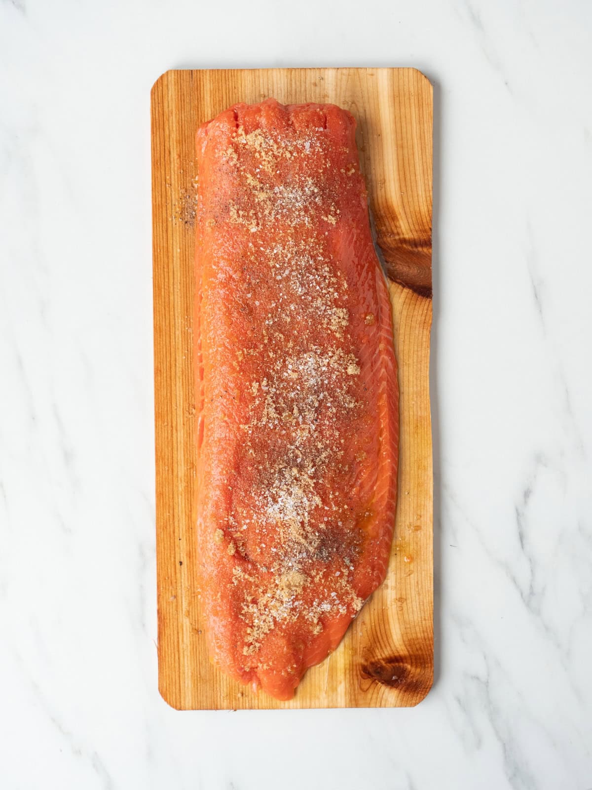 A cedar plank with salmon filet, skin side down, drizzled with olive oil and sprinkled with brown sugar, salt and pepper.