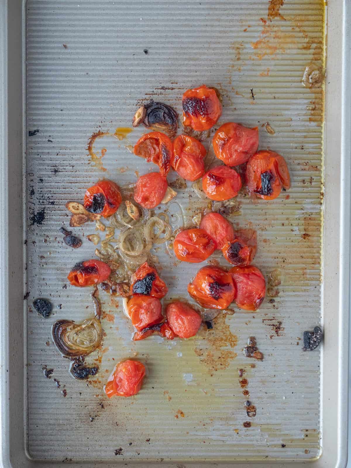 A baking sheet with charred cherry tomatoes and shallots.
