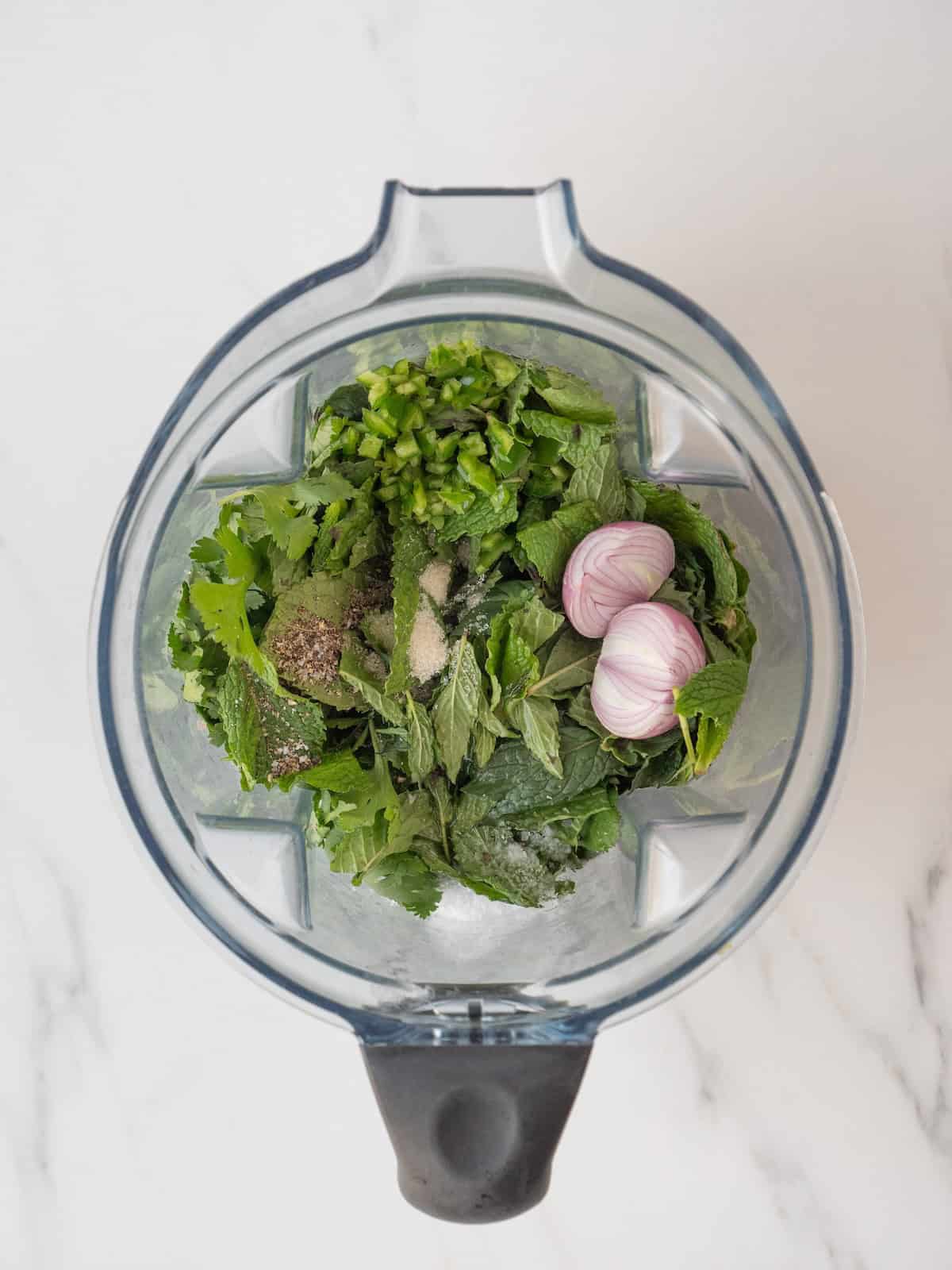 An overhead shot of a blender jar with all ingredients for cilantro mint sauce.