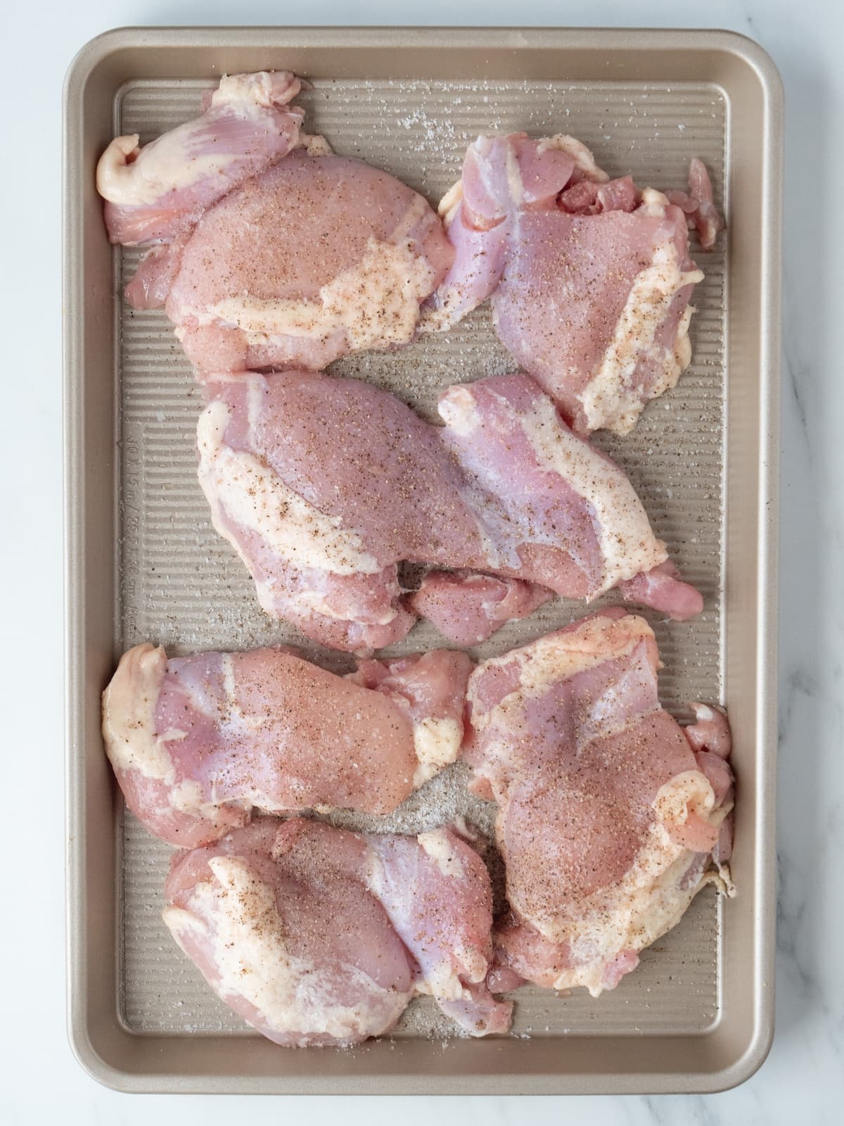 A baking sheet with chicken thighs seasoned with salt and pepper.