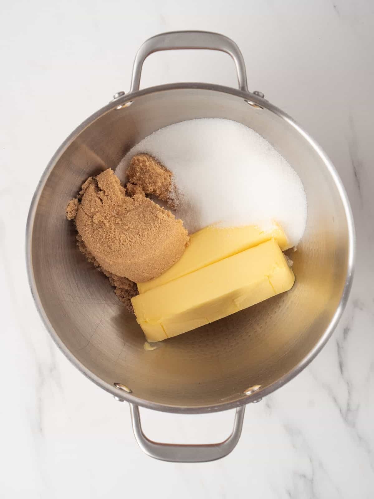 A stand mixer bowl with room temperature butter, brown sugar and white sugar.