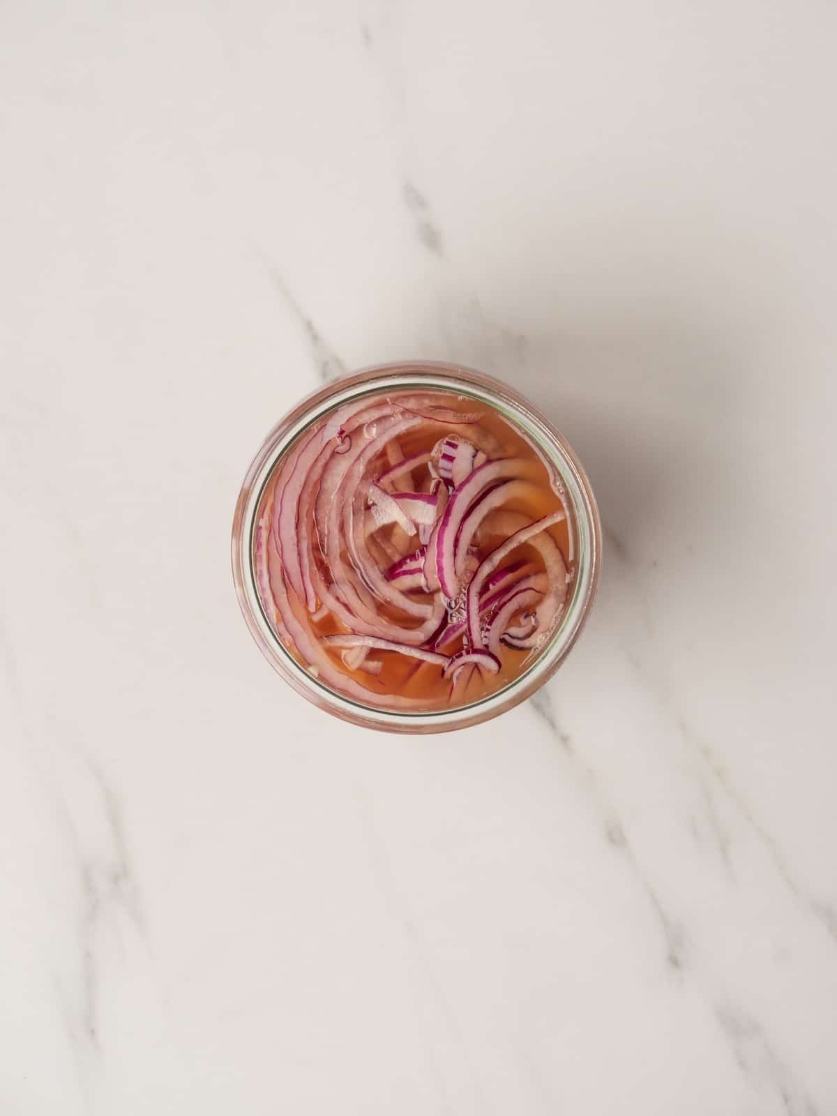 A jar with thinly sliced red onions and the pickling solution comprising vinegar, sugar and salt poured in.