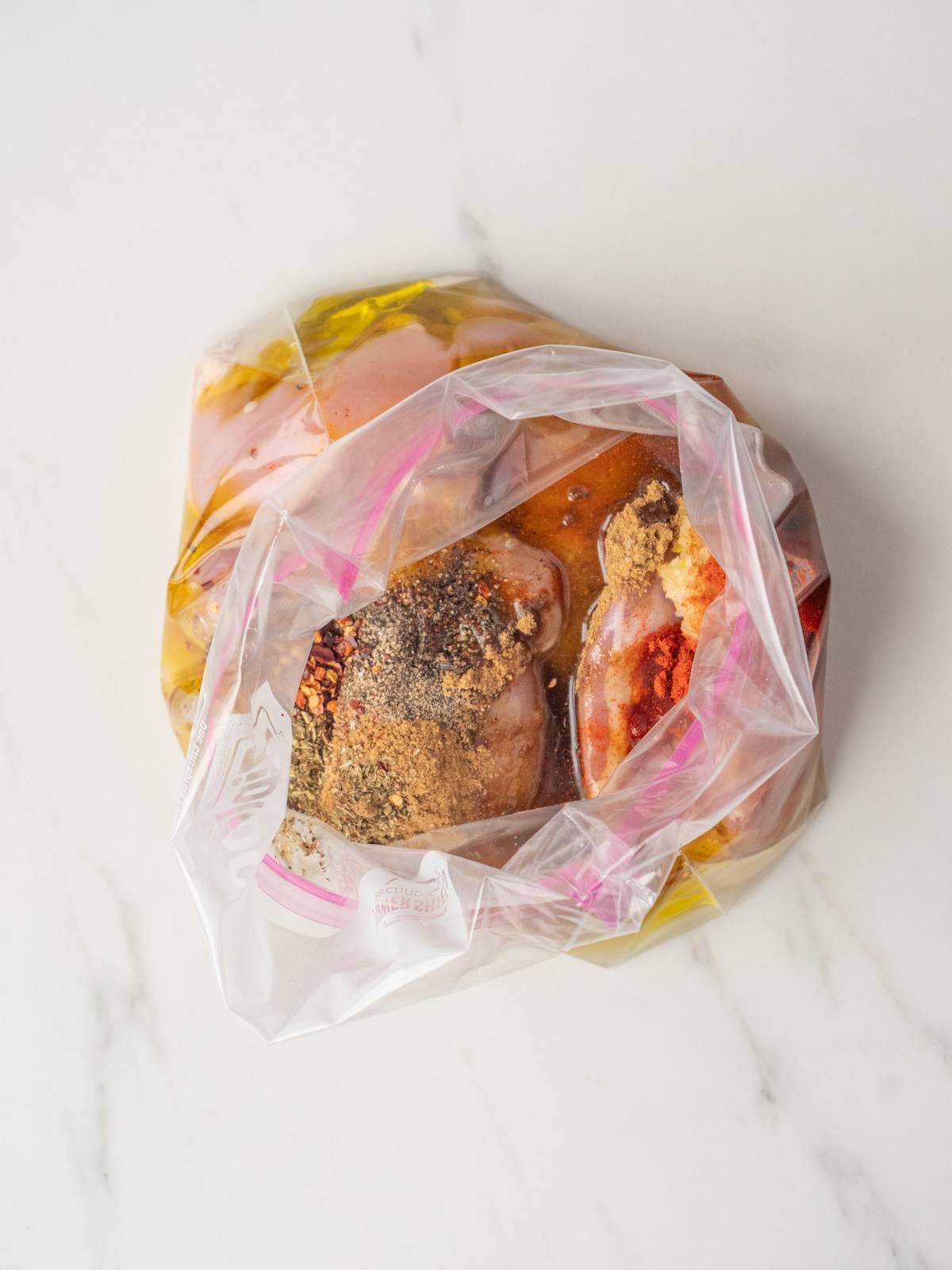 A large zip top bag with spices, olive oil and lemon added along with chicken thighs to marinade it.