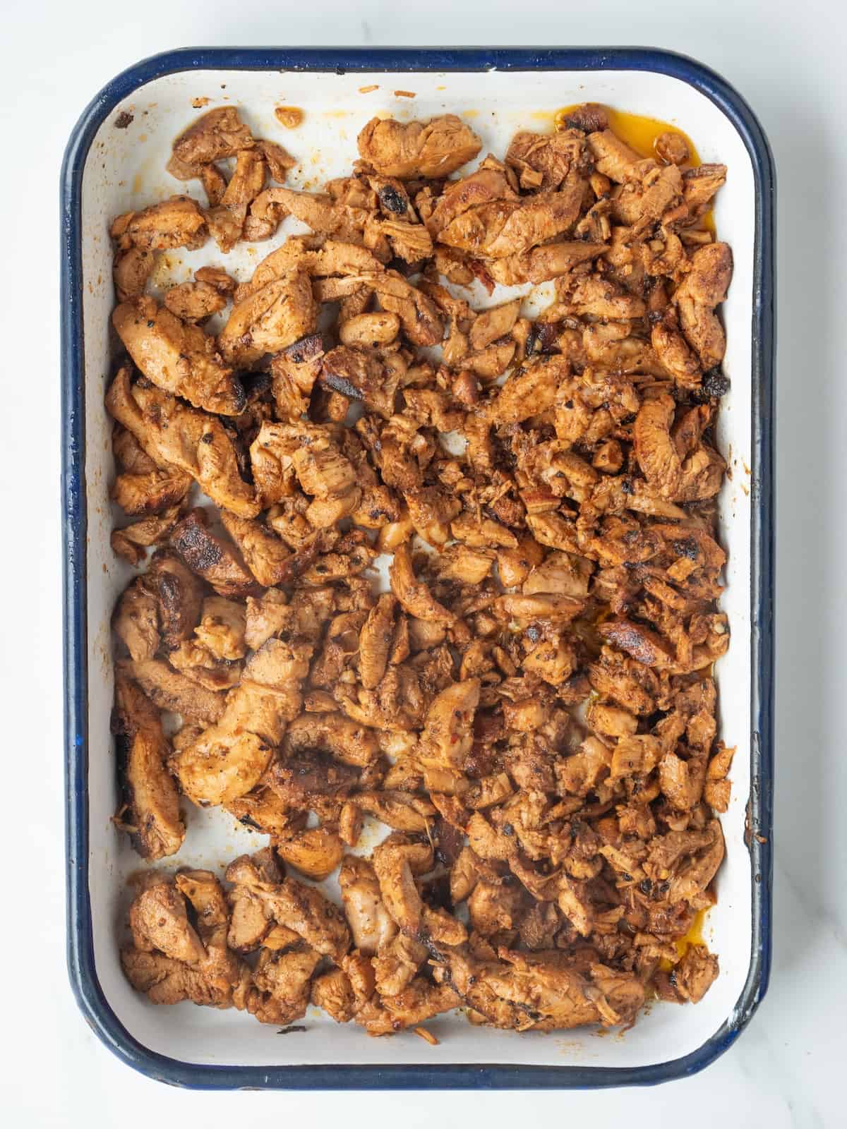 A rectangular dish with cooked chicken thighs sliced against the grain into thin strips and crisped on edges by sautéeing in the skillet for a couple minutes.