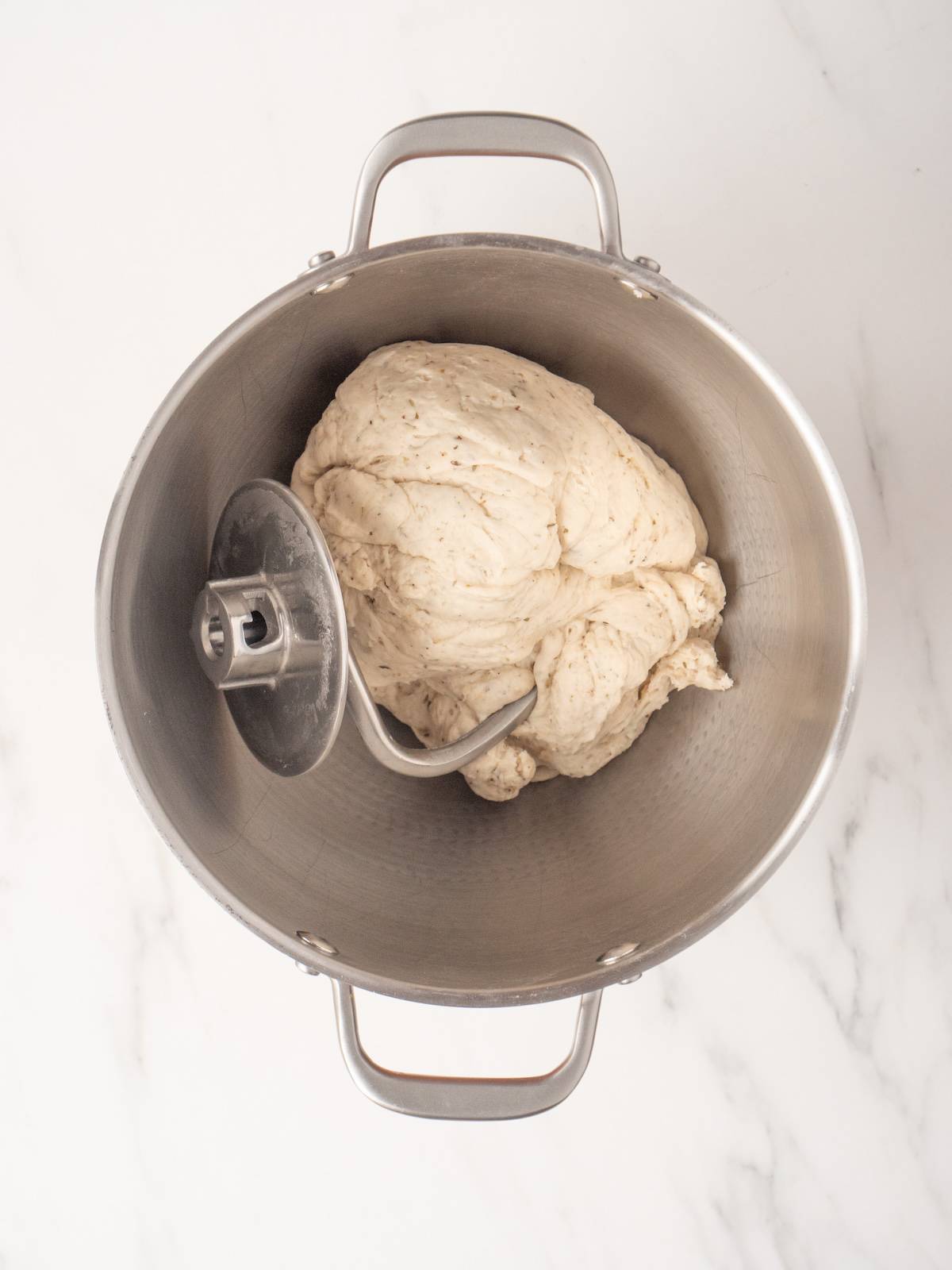 A stand mixer with pretzel dough kneaded and tangled in the dough hook attachment.