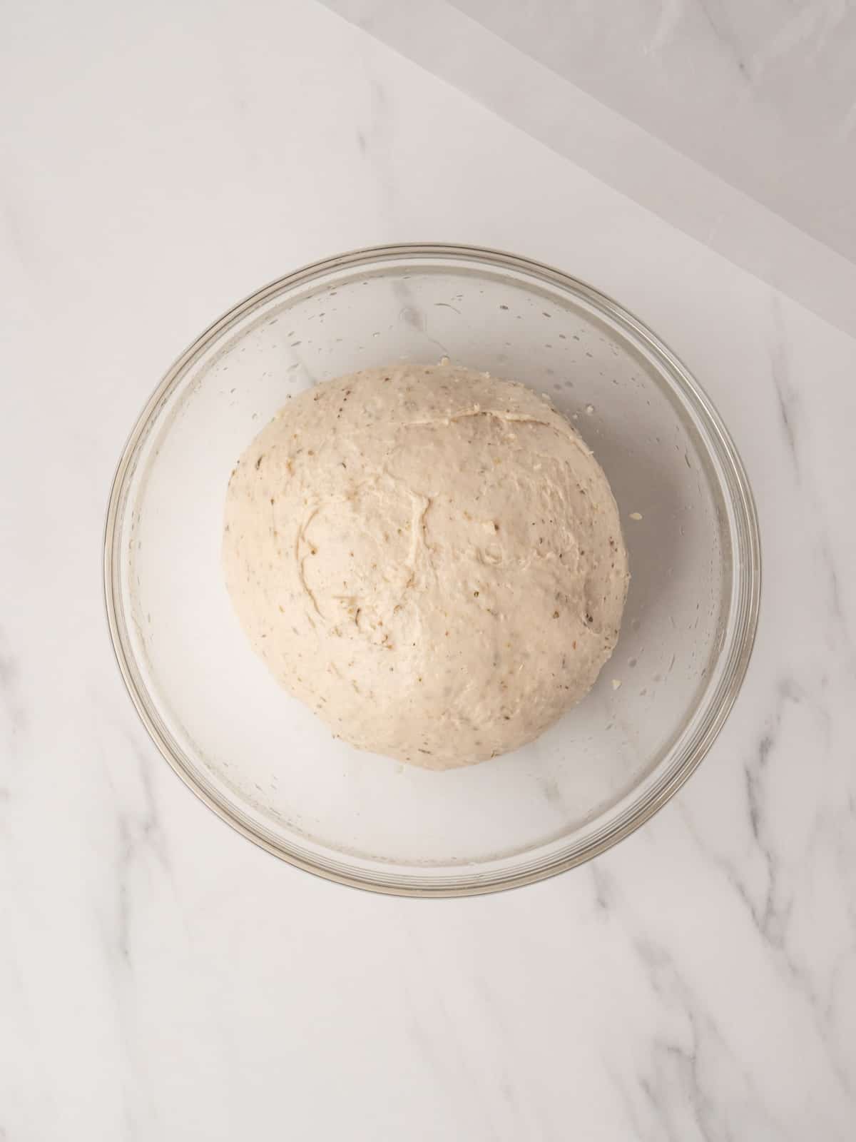 A greased large glass mixing bowl with the pretzel dough just kneaded and rolled into a ball.