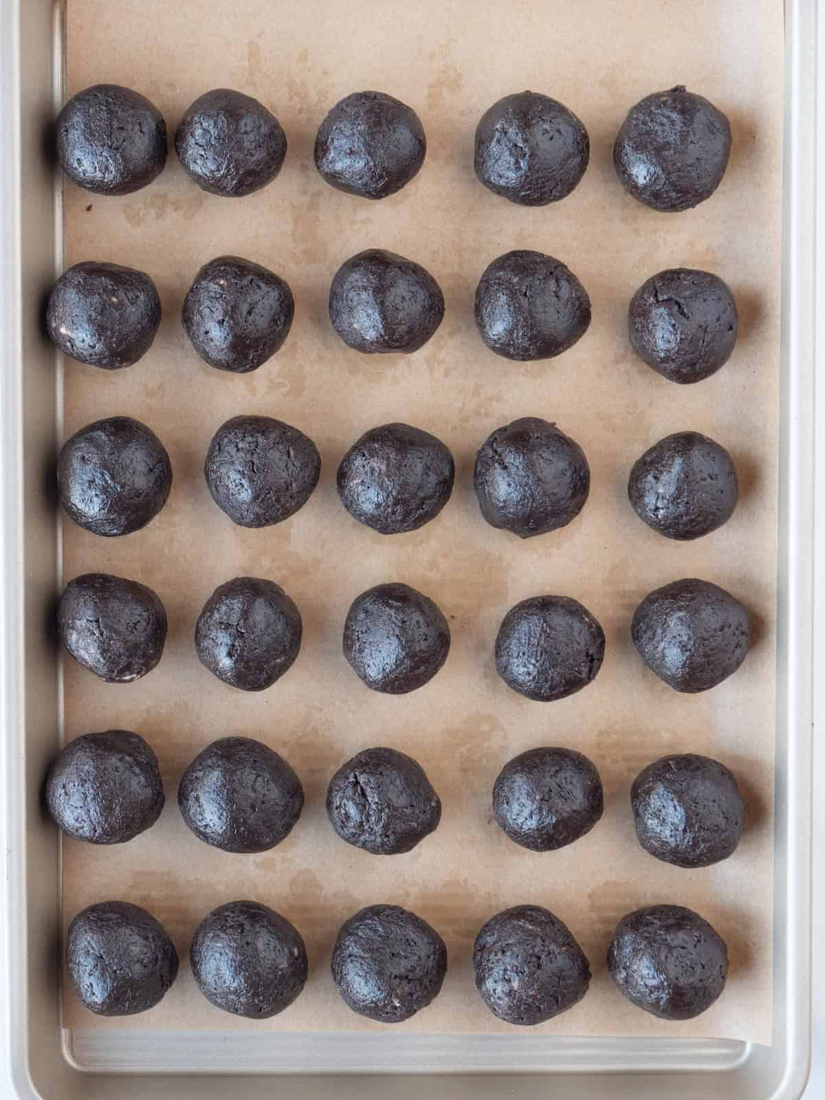 A parchment lined baking sheet with oreo and cream cheese dough rolled into two tablespoon balls and arranged in a five by six grid.