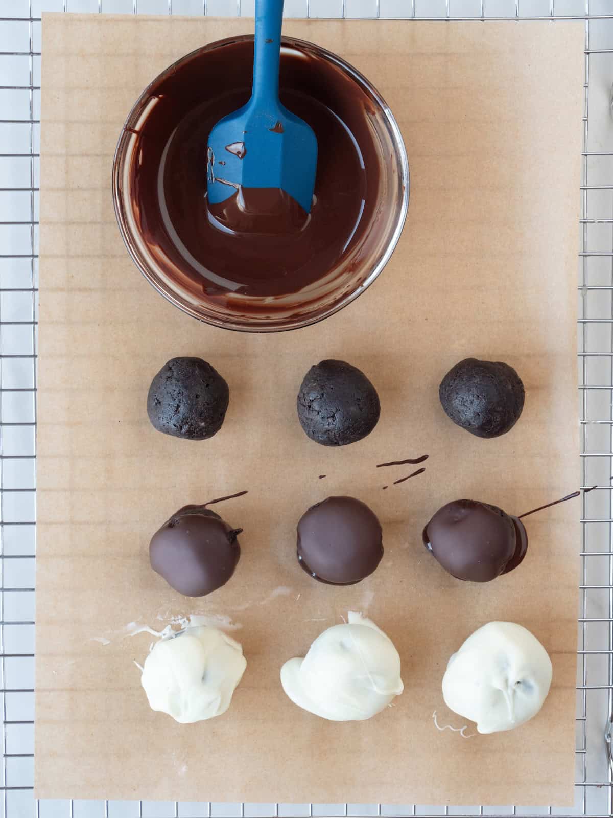 A wire rack with parchment paper on it, with a glass bowl of melted dark chocolate with a spatula in it, with nine oreo truffles, three not dipped in, three dipped in dark chocolate and three dipped in white chocolate.