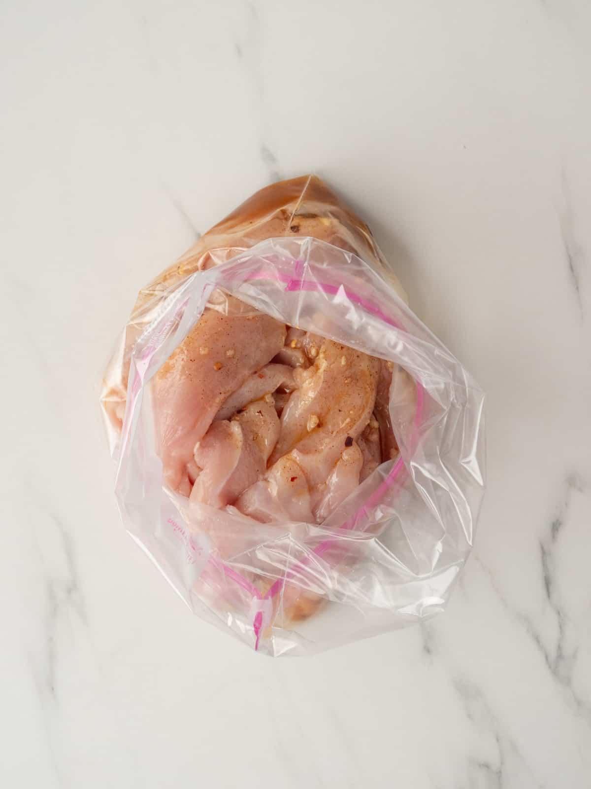 A zip top bag with chicken breasts and marinade mixed together.