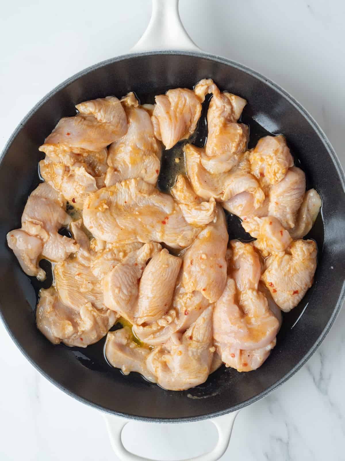 A cast iron skillet with marinated chicken being cooked.