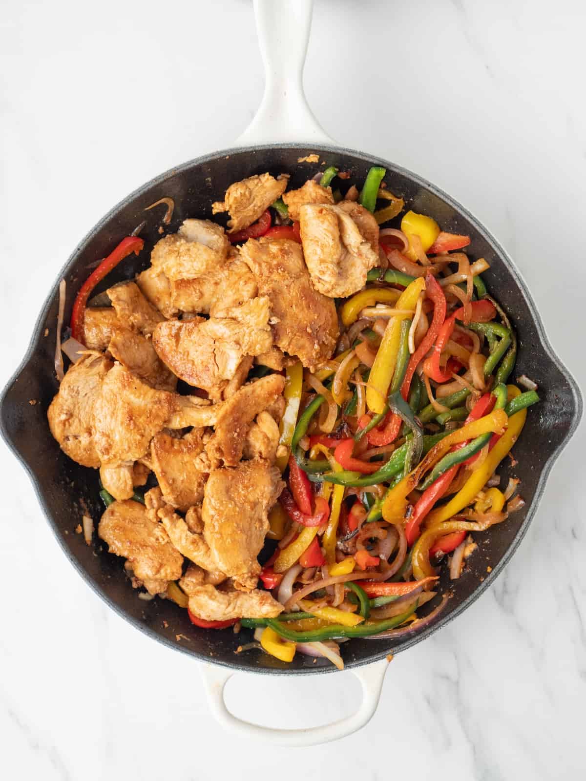 A cast iron skillet with cooked onions, bell peppers and poblano peppers, and cooked chicken added in.