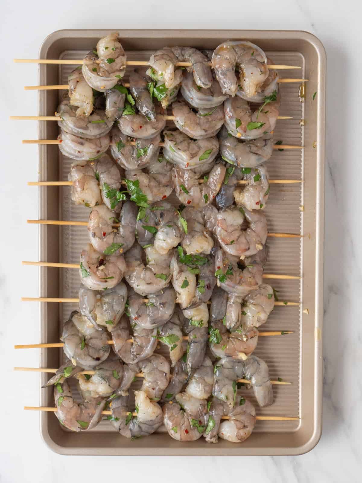A baking sheet with raw seasoned shrimp threaded on to skewers.