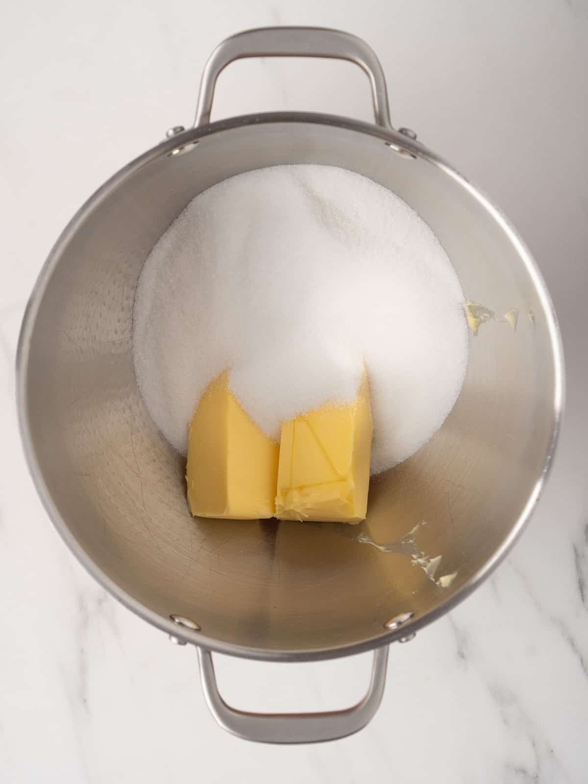 A stand mixer bowl with white sugar and room temperature butter, ready to be creamed together.