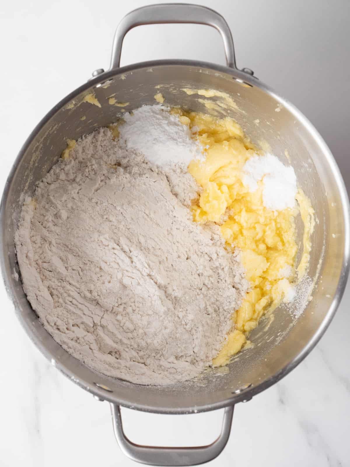 A stand mixer bowl with creamed butter, sugar and eggs mixture, with the dry ingredients of flour, baking soda, salt and cream of tartar added.