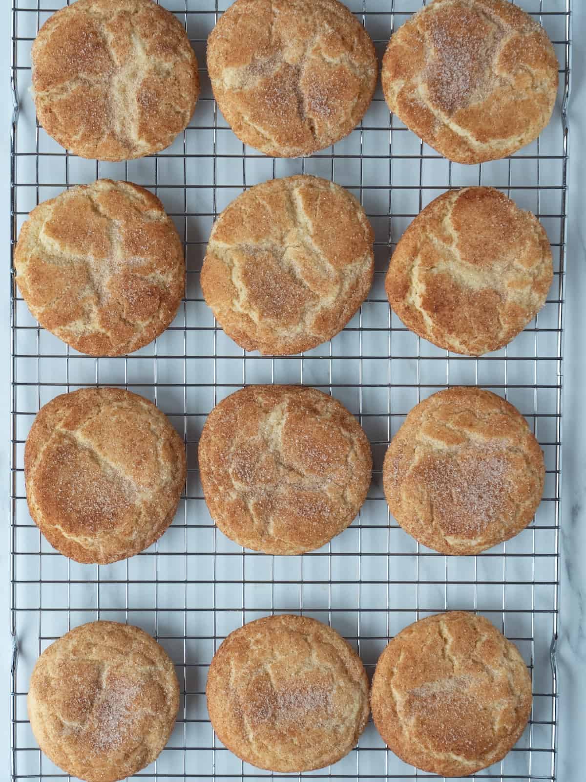 A wire rack with twelve snickerdoodle cookies in a grid, being cooled after baking.