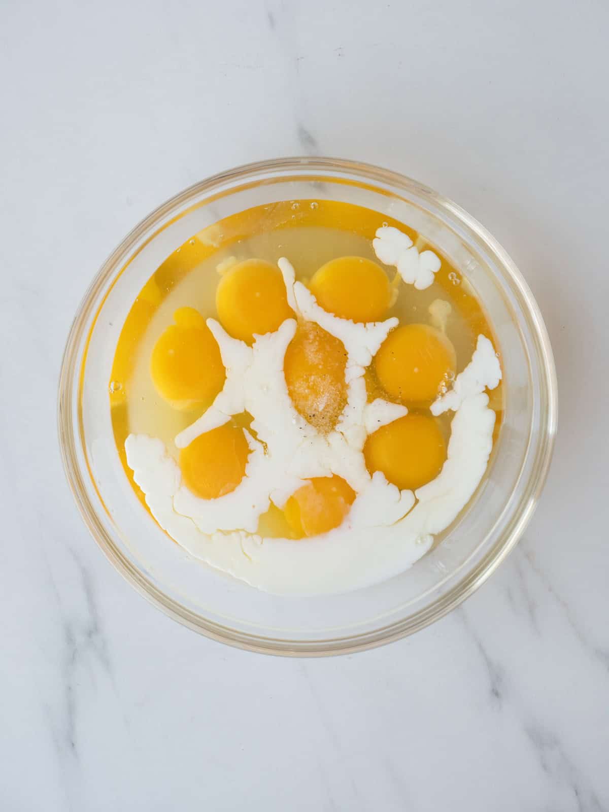 A glass mixing bowl with cracked eggs, milk and a pinch of salt.