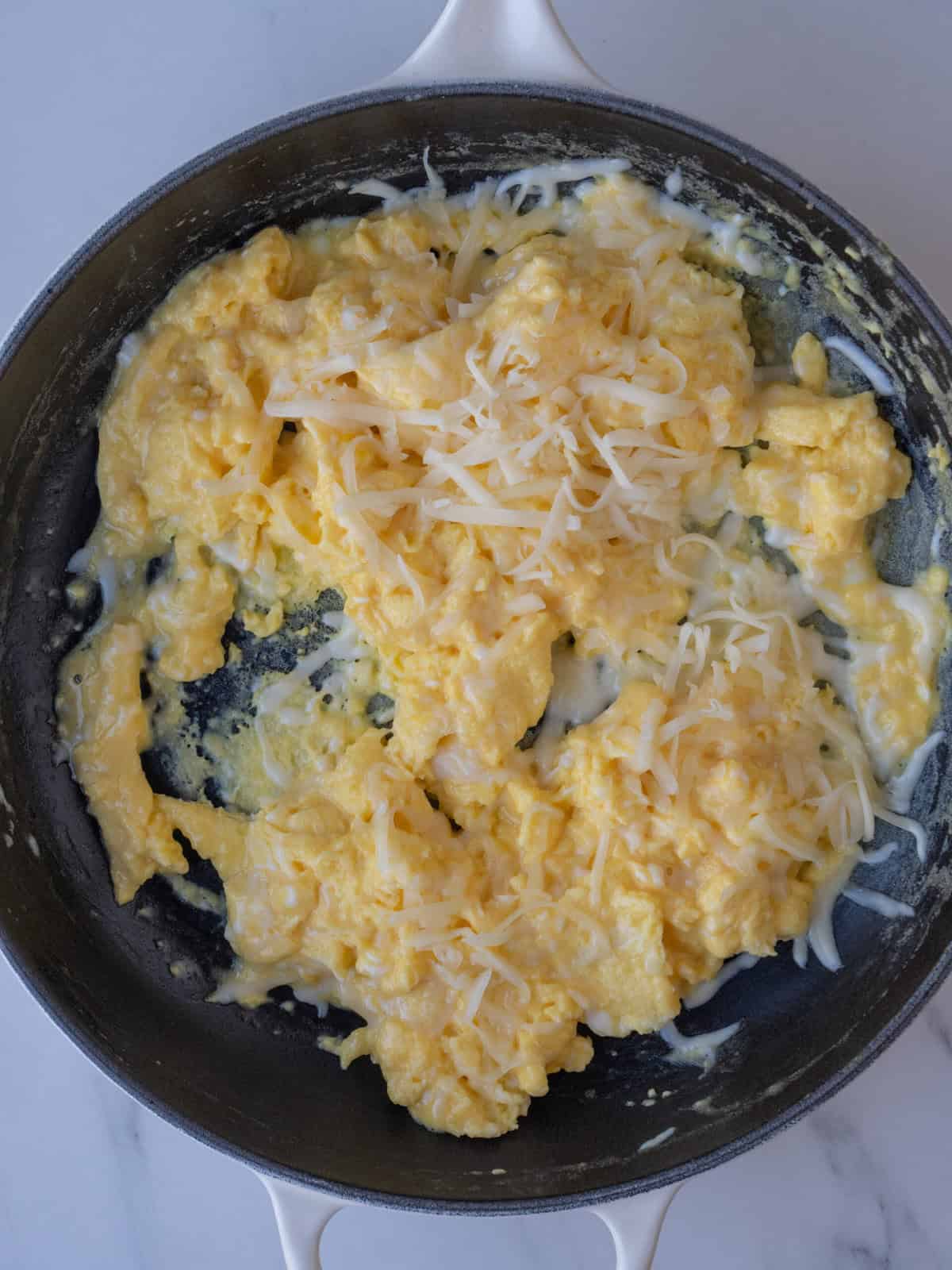 A nonstick pan with scrambled eggs being cooked and shredded fontina just added.
