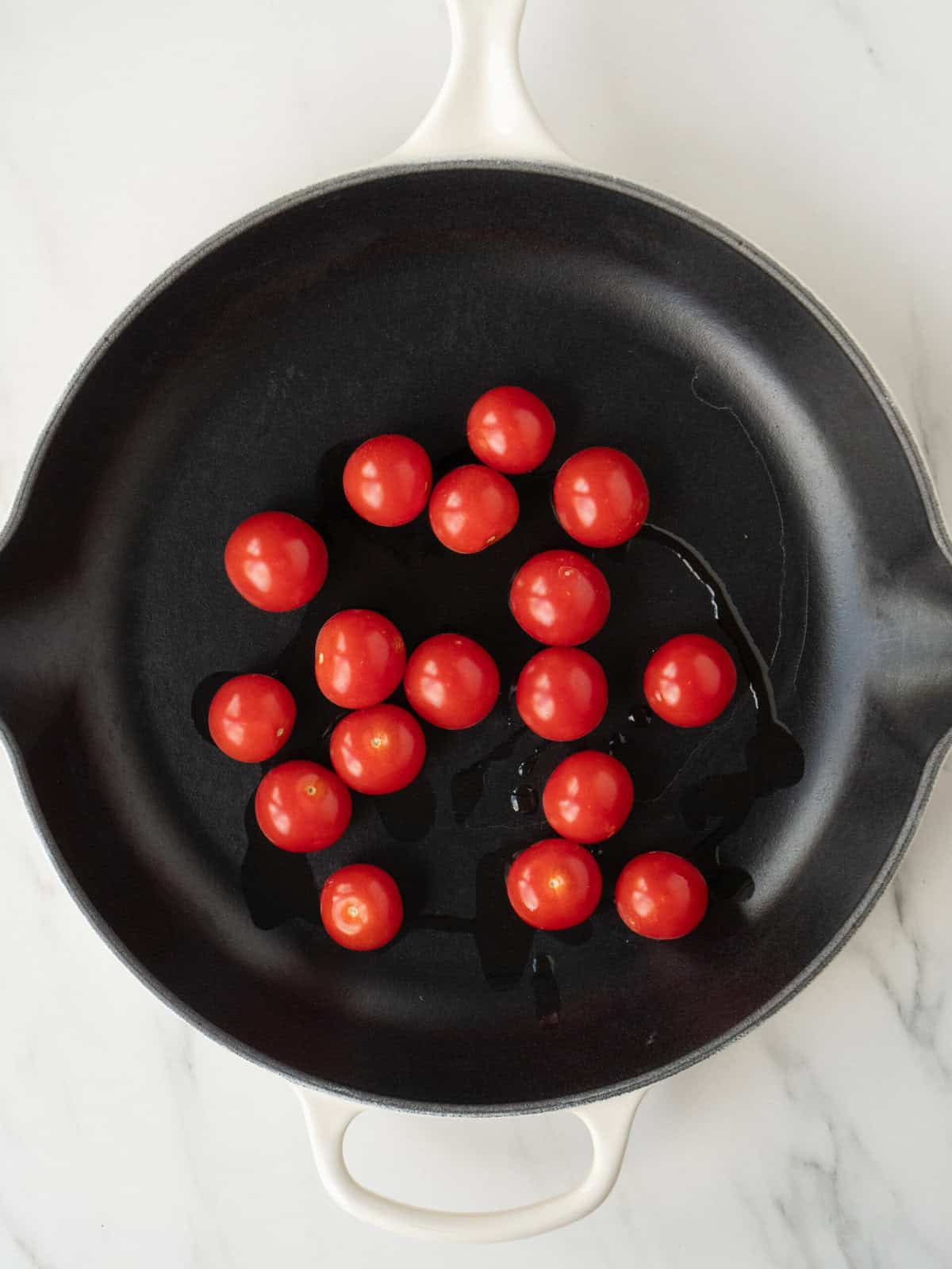 A non stick pan with oil and cherry tomatoes.