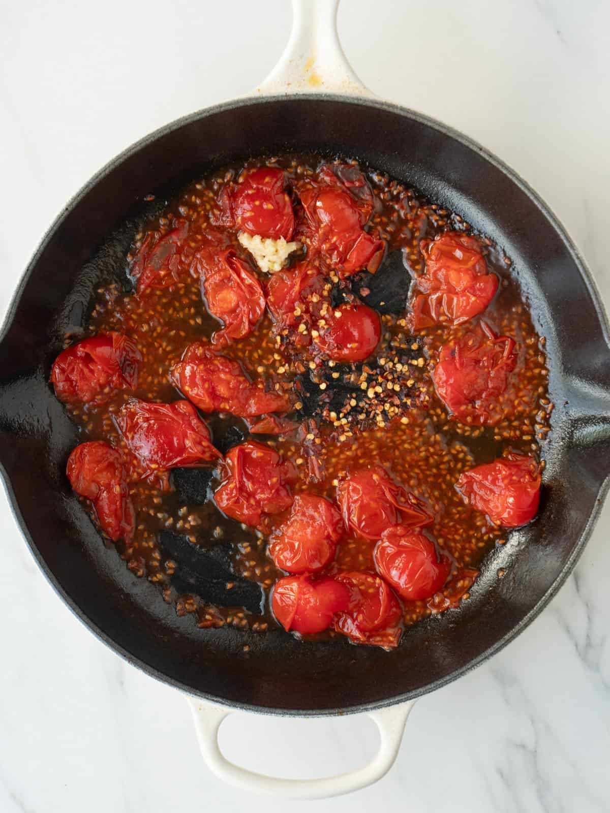 A non stick pan with cherry tomatoes starting to blister with red pepper flakes just added.