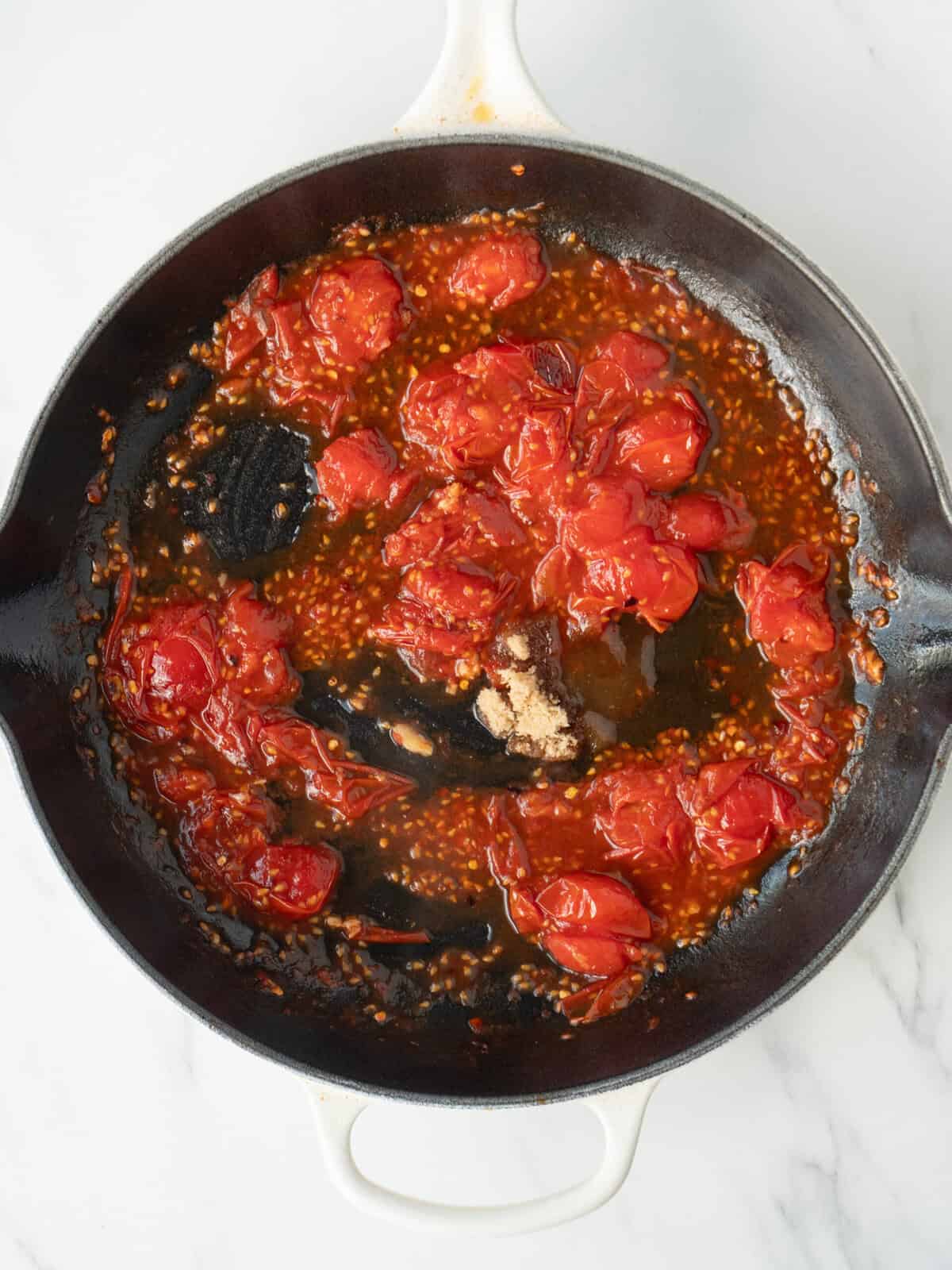 A non stick pan with cherry tomatoes being cooked, partially blistered and smashed with garlic just added.