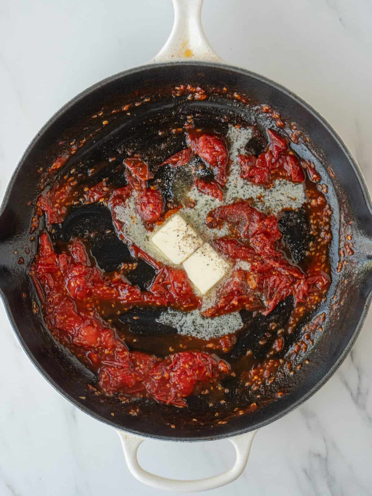 A non stick pan with cherry tomatoes being cooked, and butter just added.