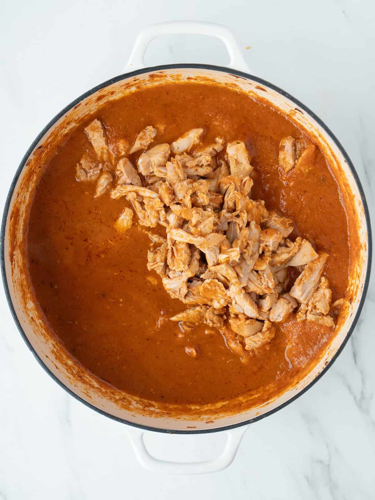 A dutch oven with the chipotle tomato sauce, and cooked chicken cut into strips added, which is the final chicken tinga.