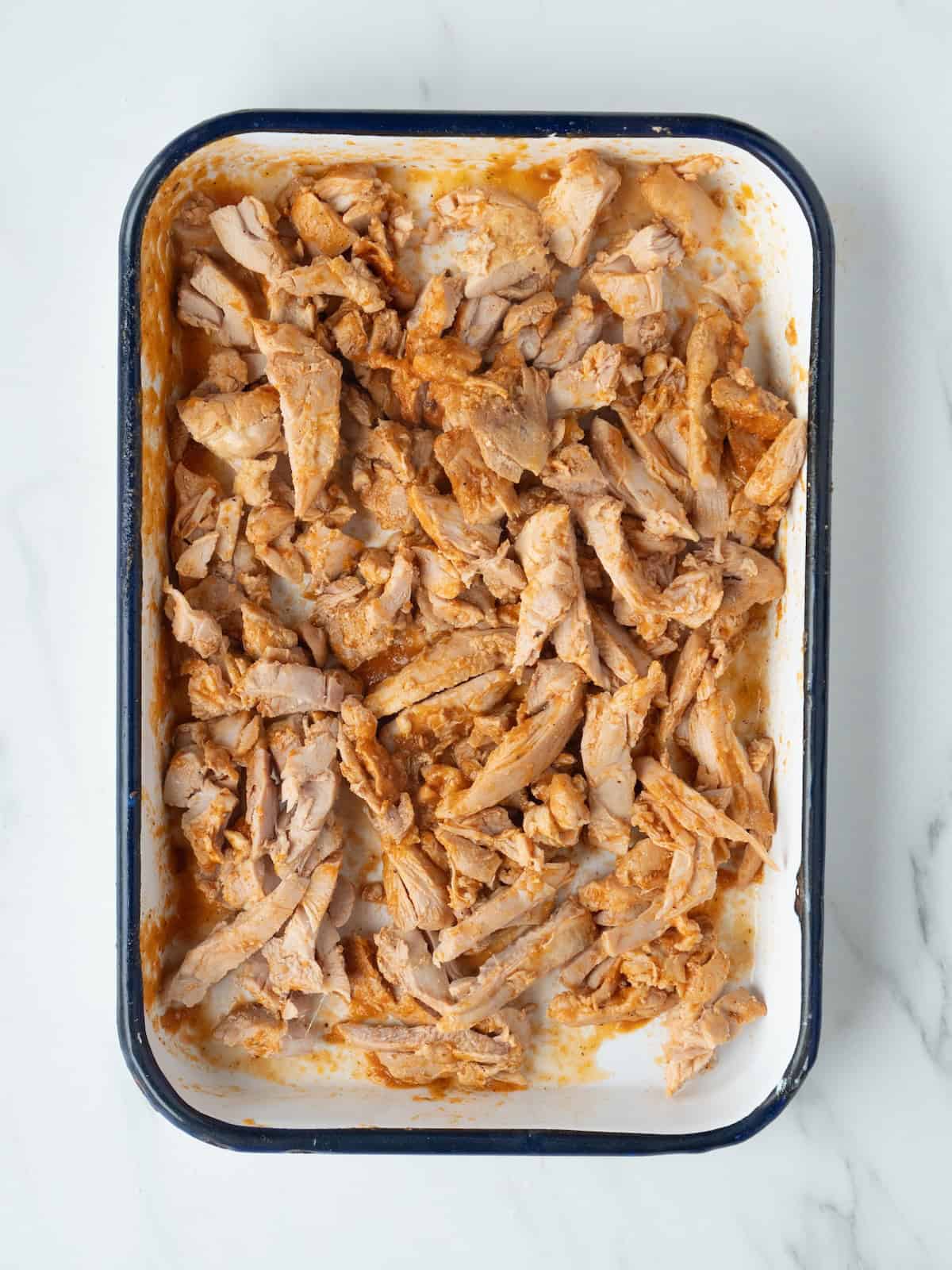 A rectangular dish with cooked chicken thighs cut into strips.