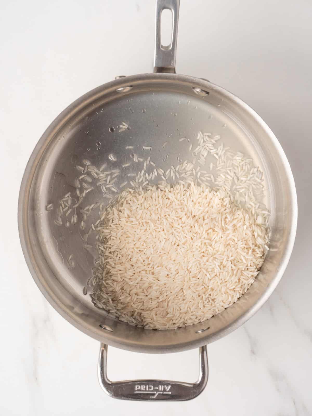 A saucepan with white basmati rice being toasted with lime juice and olive oil.