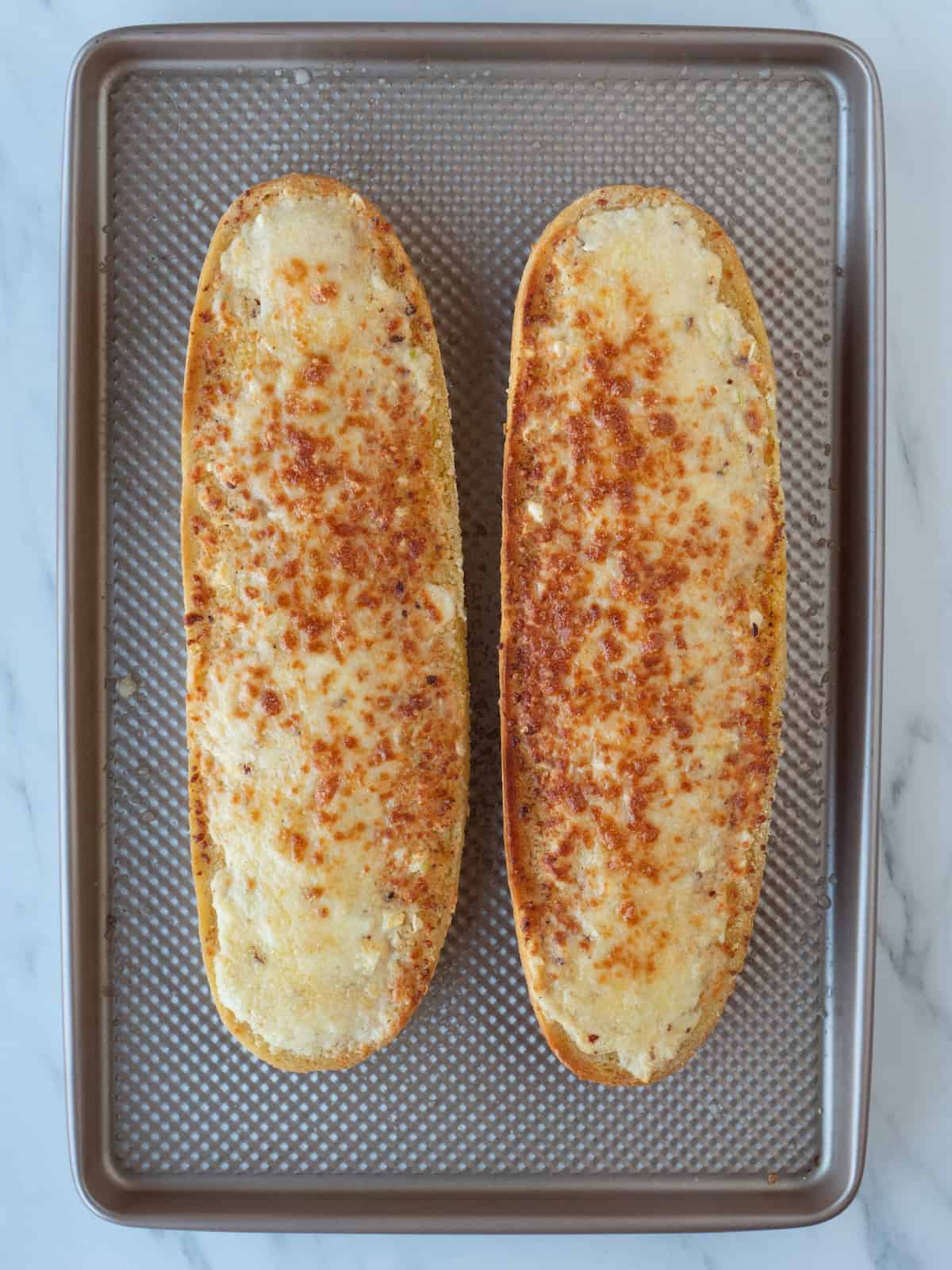 Horizontally cut halves of a bread loaf on a baking sheet, with the butter cheese garlic red pepper flakes mixture on them baked till golden in color, fresh out of the oven.