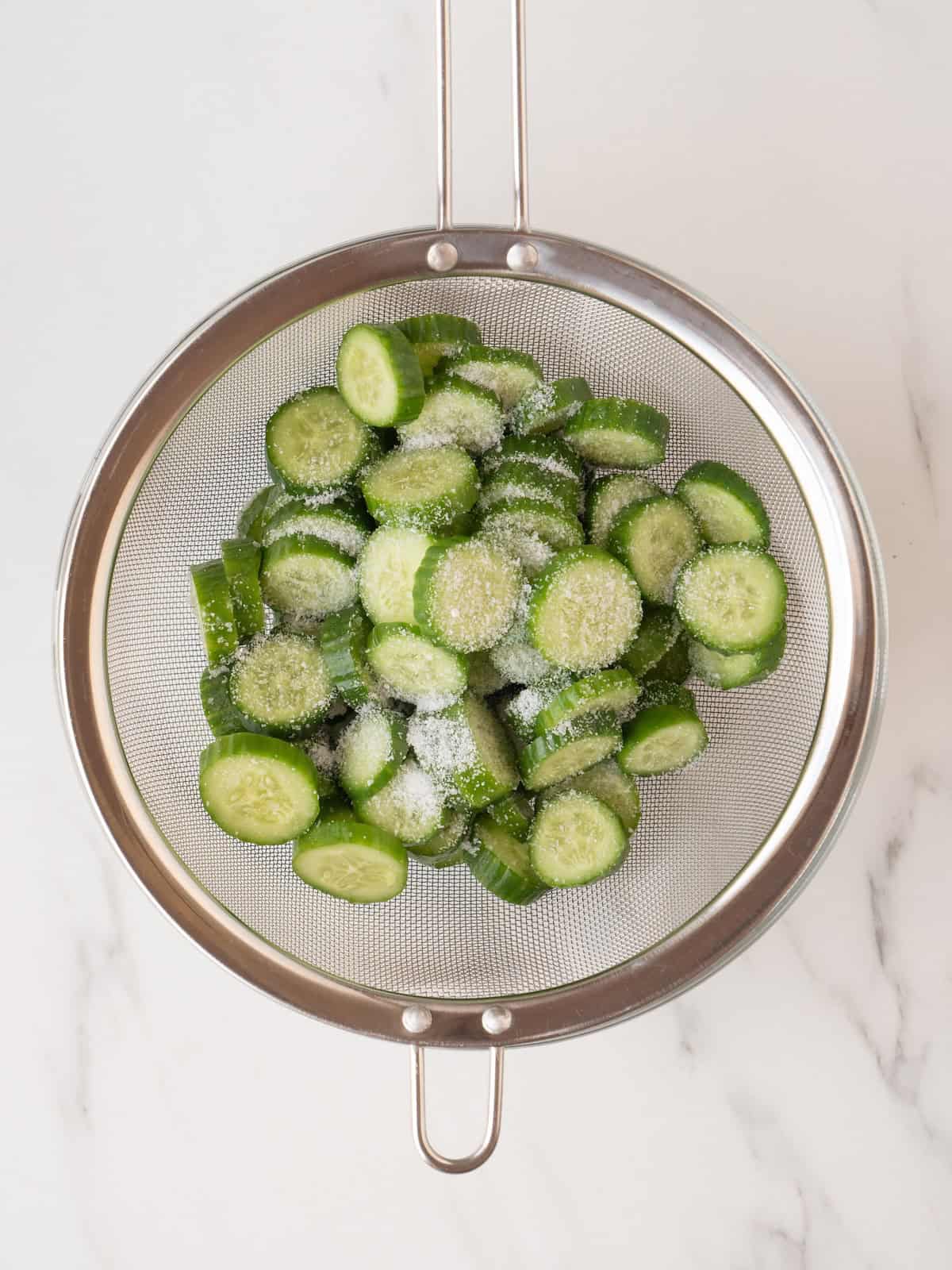 A large sieve with sliced cucumbers sprinkled with kosher salt.