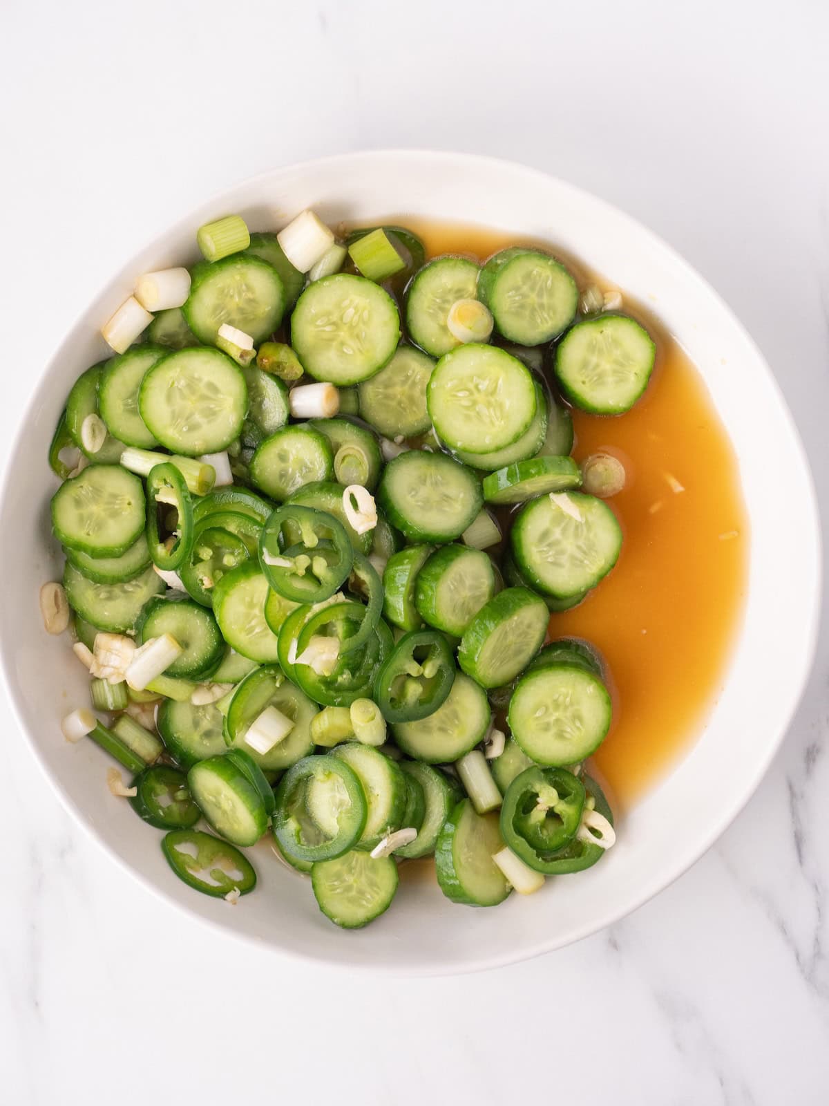 A bowl with sliced cucumbers and its seasonings, soaked in a liquid mixture containing rice vinegar, sesame oil, honey and soy sauce.