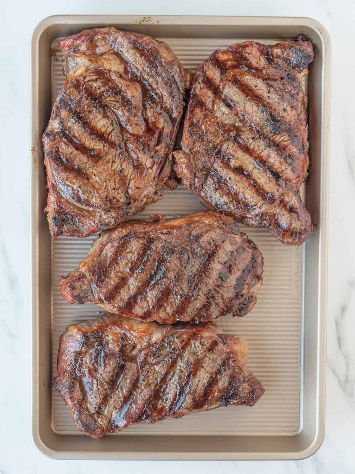 A baking sheet with four grilled rib eye steaks.