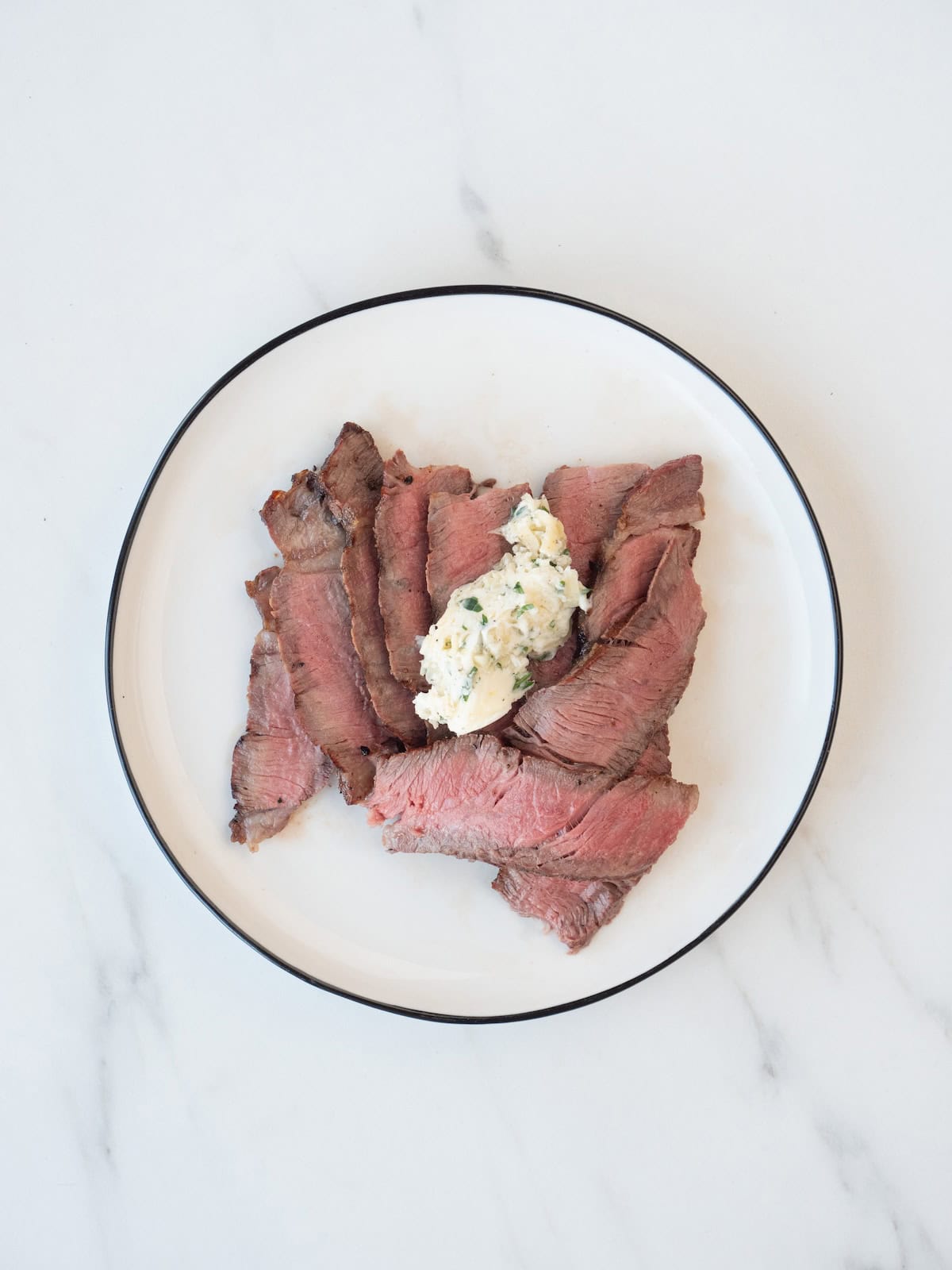 A plate with sliced grilled rib eye steak, and a dollop of compound butter on top.