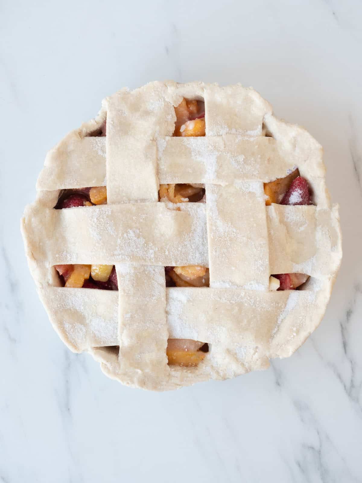 A pie pan lined with pie dough and filled with the strawberry-peach filling, and sealed on top with a lattice that is made out of pie dough cut intro strips and brushed with egg white wash.