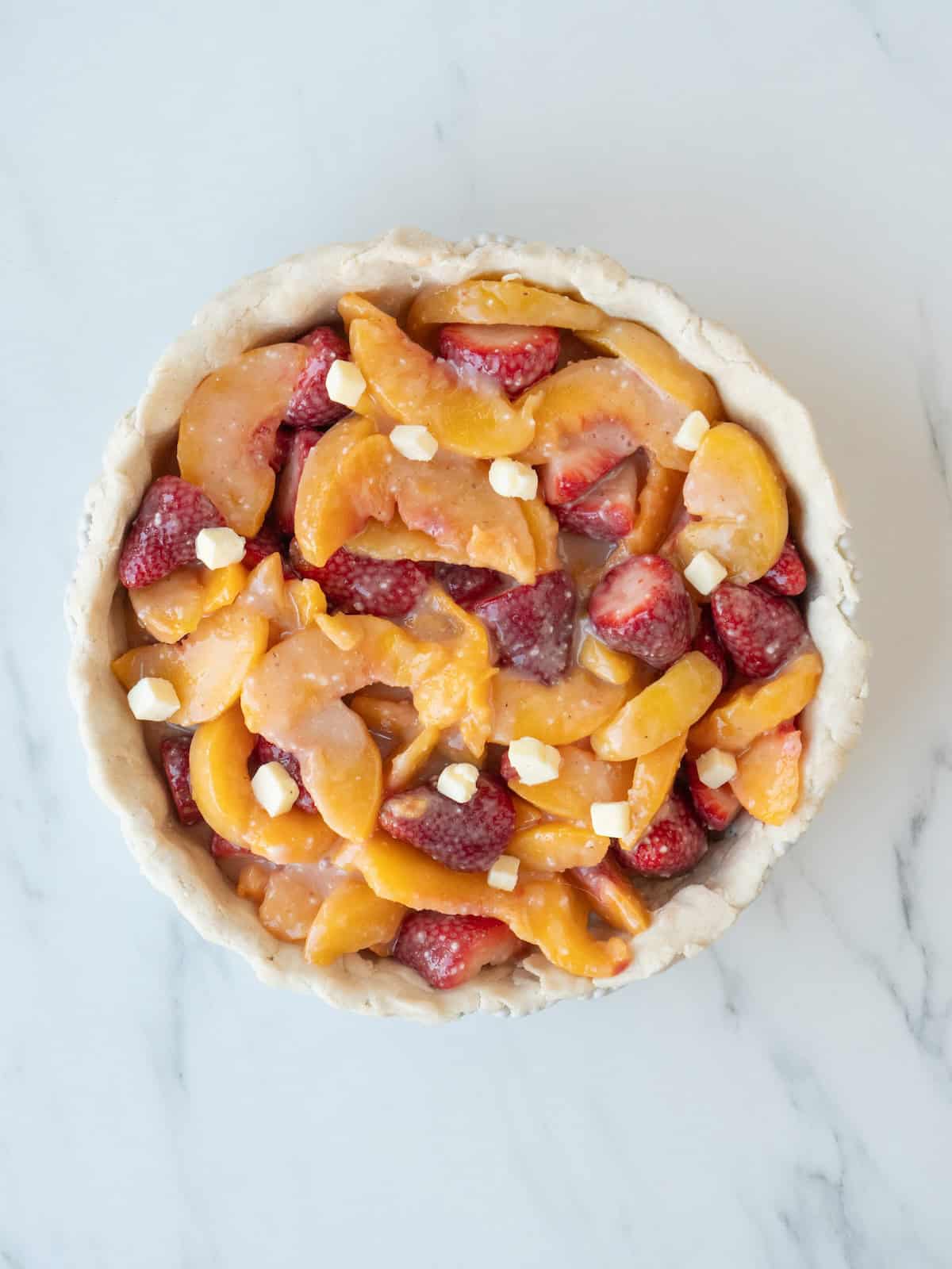 A pie pan lined with pie dough and filled with the strawberry-peach filling, and then dotted with little pieces of butter.